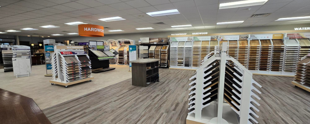 Jim's Carpet One flooring showroom displaying various hardwood and waterproof flooring samples on racks and shelves.